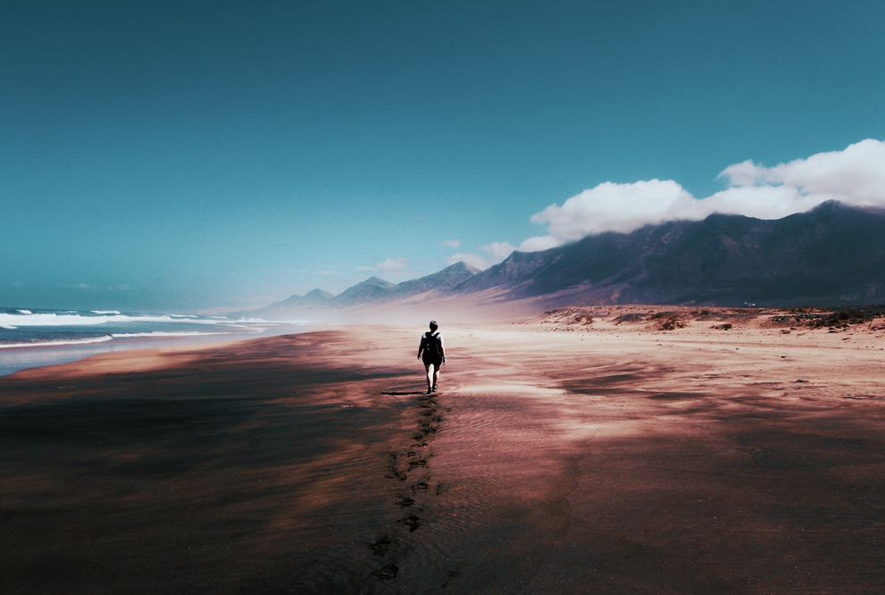 una persona caminando por la playa con montañas al fondo